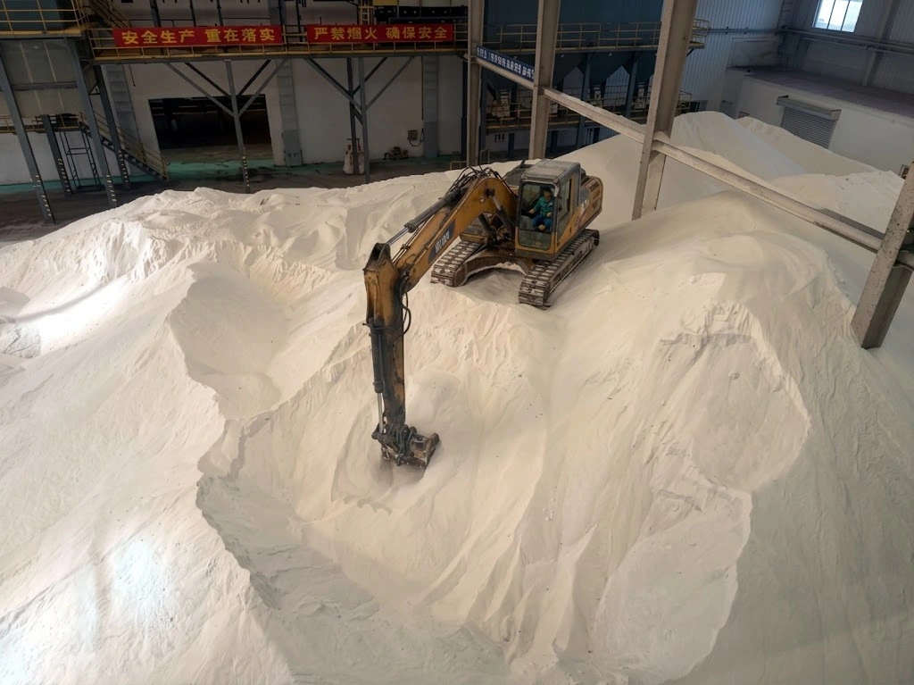 Excavator working across a white bulk cargo stockpile in a warehouse