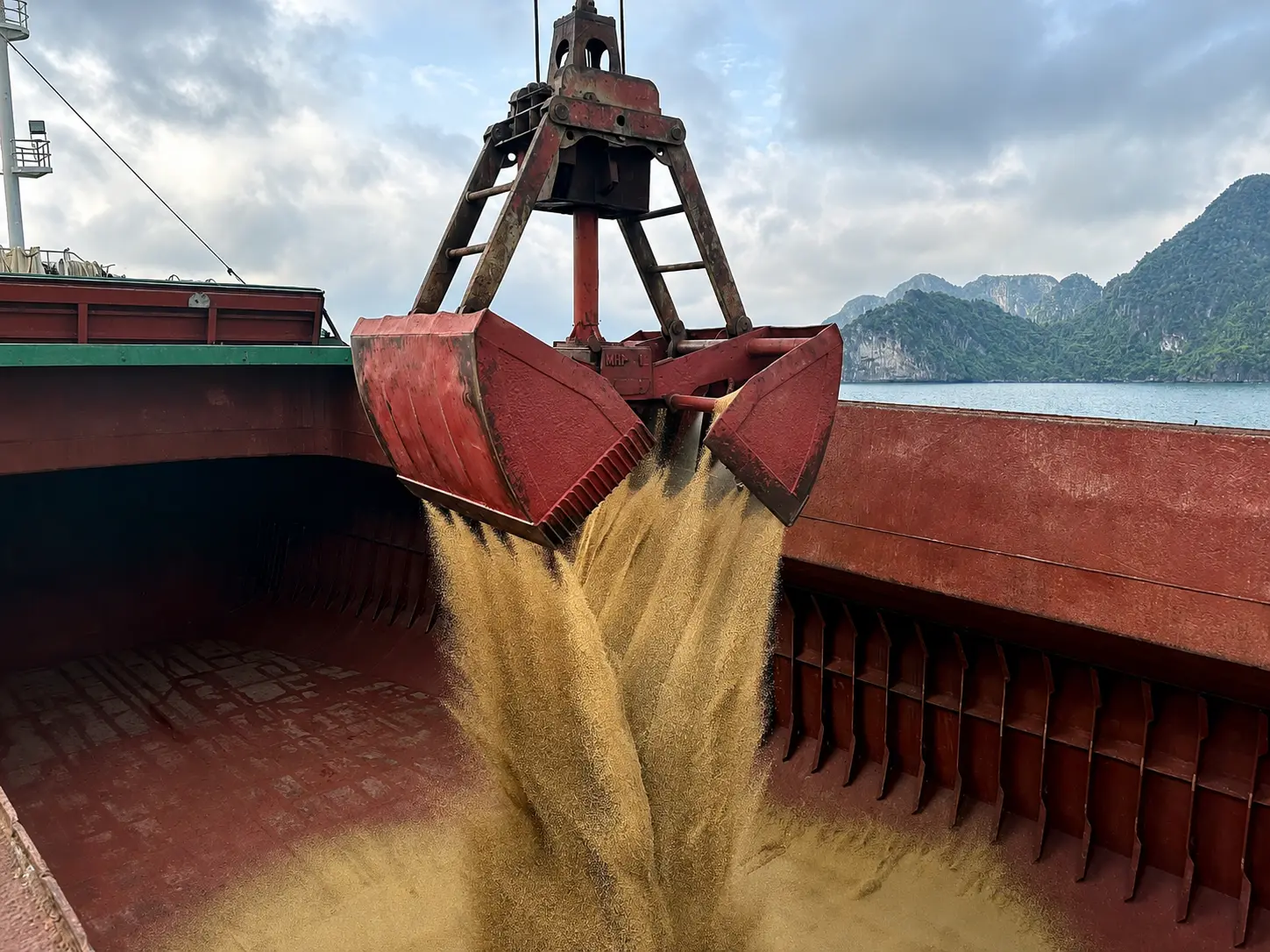 Grab bucket unloading yellow granular bulk cargo into a vessel hold